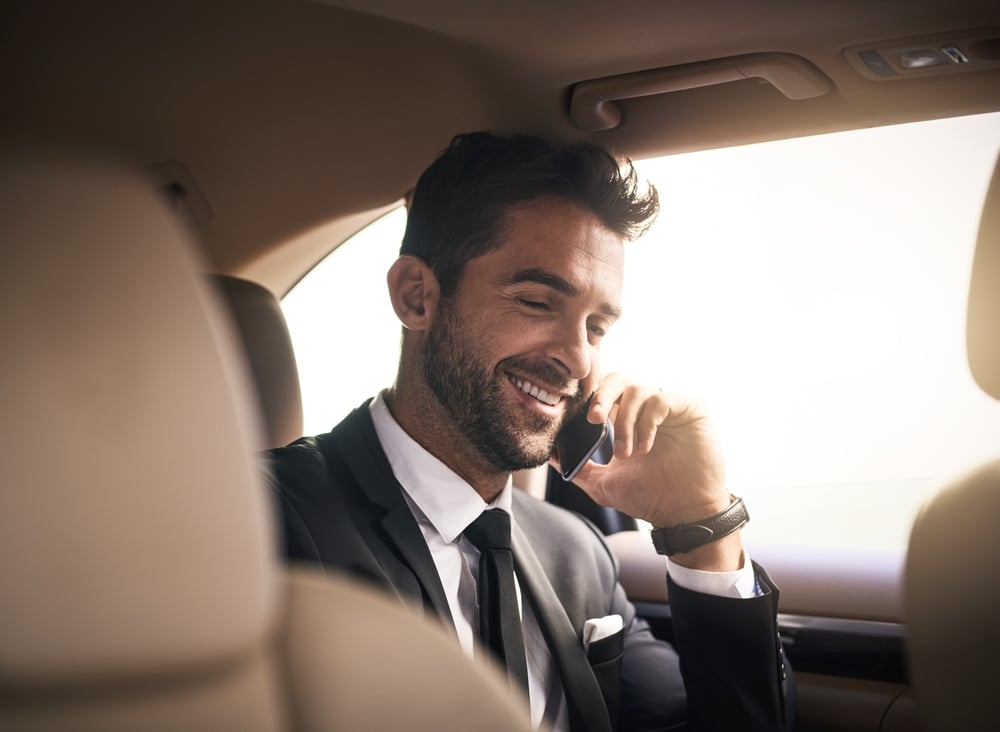 Homme d'affaires en voiture de luxe passant un appel Homme d'affaires souriant en costume téléphonant à l'arrière d'une voiture de luxe.